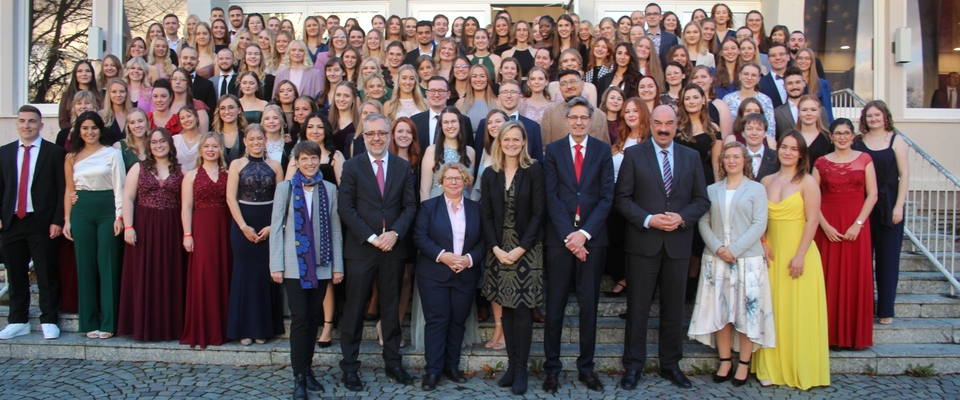 Es wird ein Gruppenbild gezeigt, auf dem alle Diplomandinnen und Diplomanden zu sehen sind. In der vorderen Reihe sind von link nach rechts zu sehen: Caroline Ströttchen (Abteilungsleiterin Justizvollzug), Dr. Alexander Meyer (Direktor FHR), Staatssekretärin Dr. Daniela Brückner, Gudrun Schäpers (Präsidentin OLG Hamm), Dr. Werner Richter (Präsident OLG Düsseldorf), Dr. Bernd Scheiff (Präsident OLG Köln)